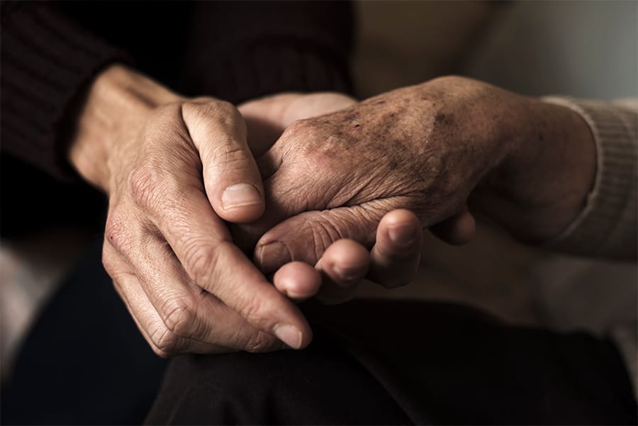 A close-up of two people holding hands, with a younger hand gently supporting an older hand