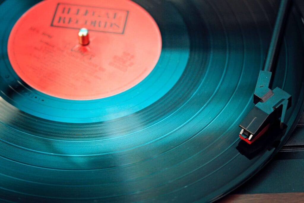 A close-up view of a vinyl record spinning on a turntable, with the needle positioned on the grooves and a red label at the center.