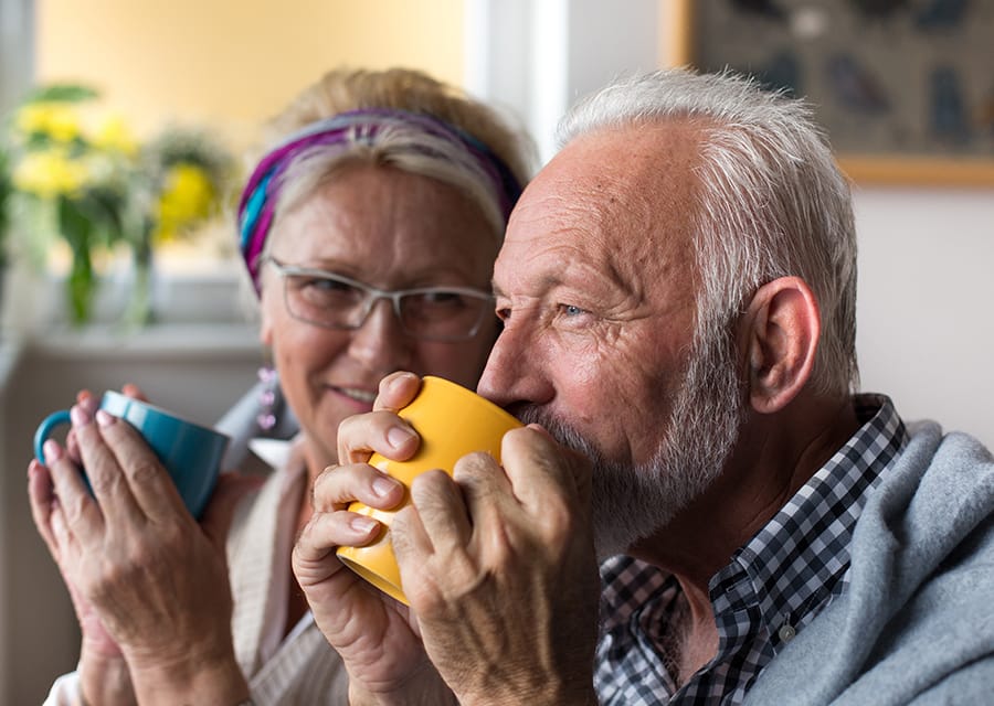 Happy senior couple drinking tea covered with blanket at home