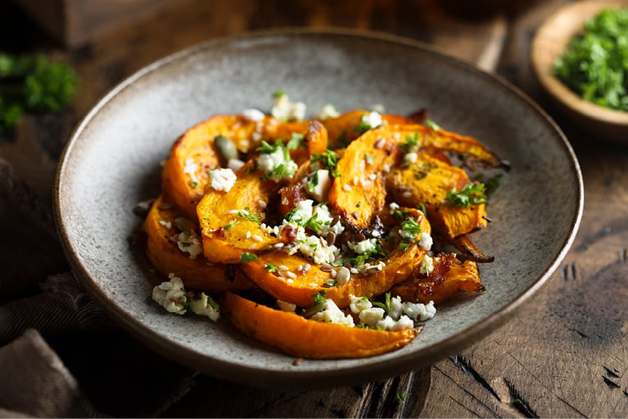 A plate of roasted butternut squash slices topped with crumbled cheese and fresh herbs.