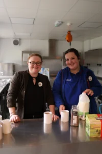Two assistants from tesco stood pouring drinks at the Knowle and Dorridge memory cafe