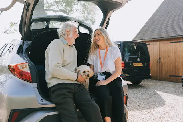 elderly man and carer sitting in the boot of car