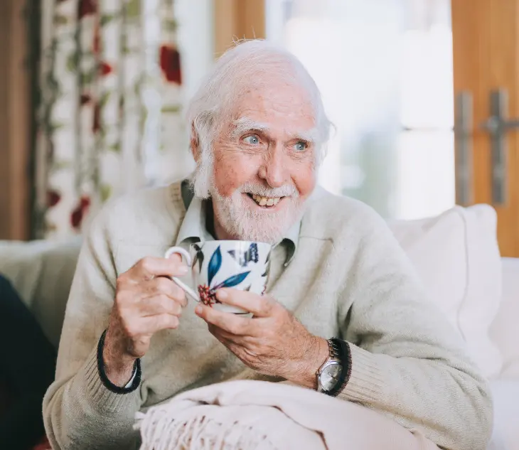 An older gentleman sat smiling while holding a cup of tea