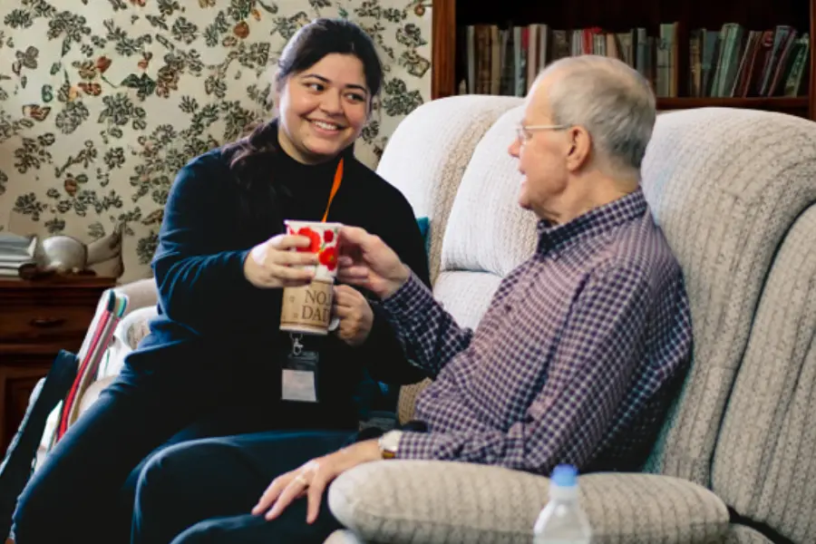 A caregiver handing her elderly client a cup of tea