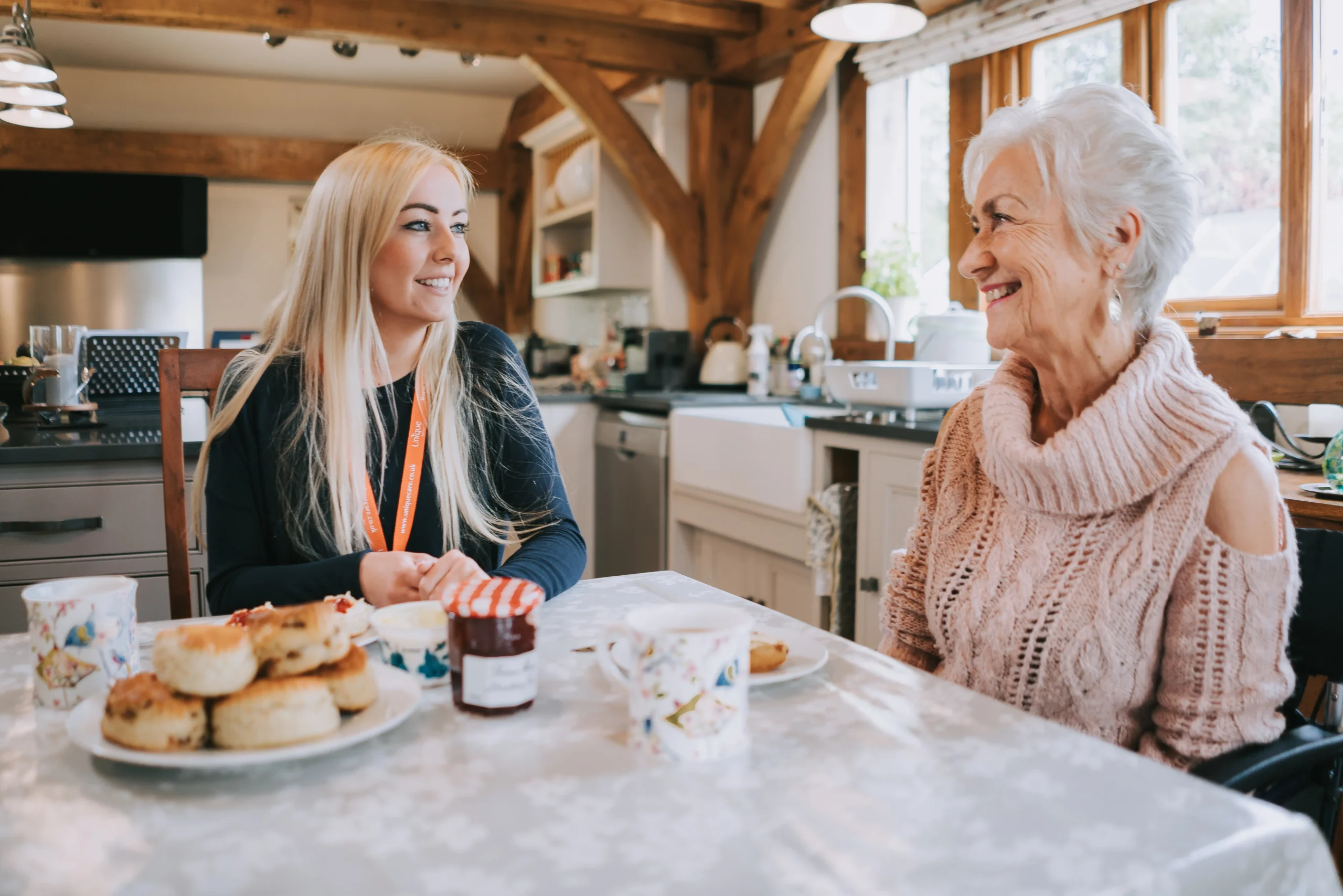 An elderly lady and her carergiver smiling warmly at each other while enjoying afternoon tea