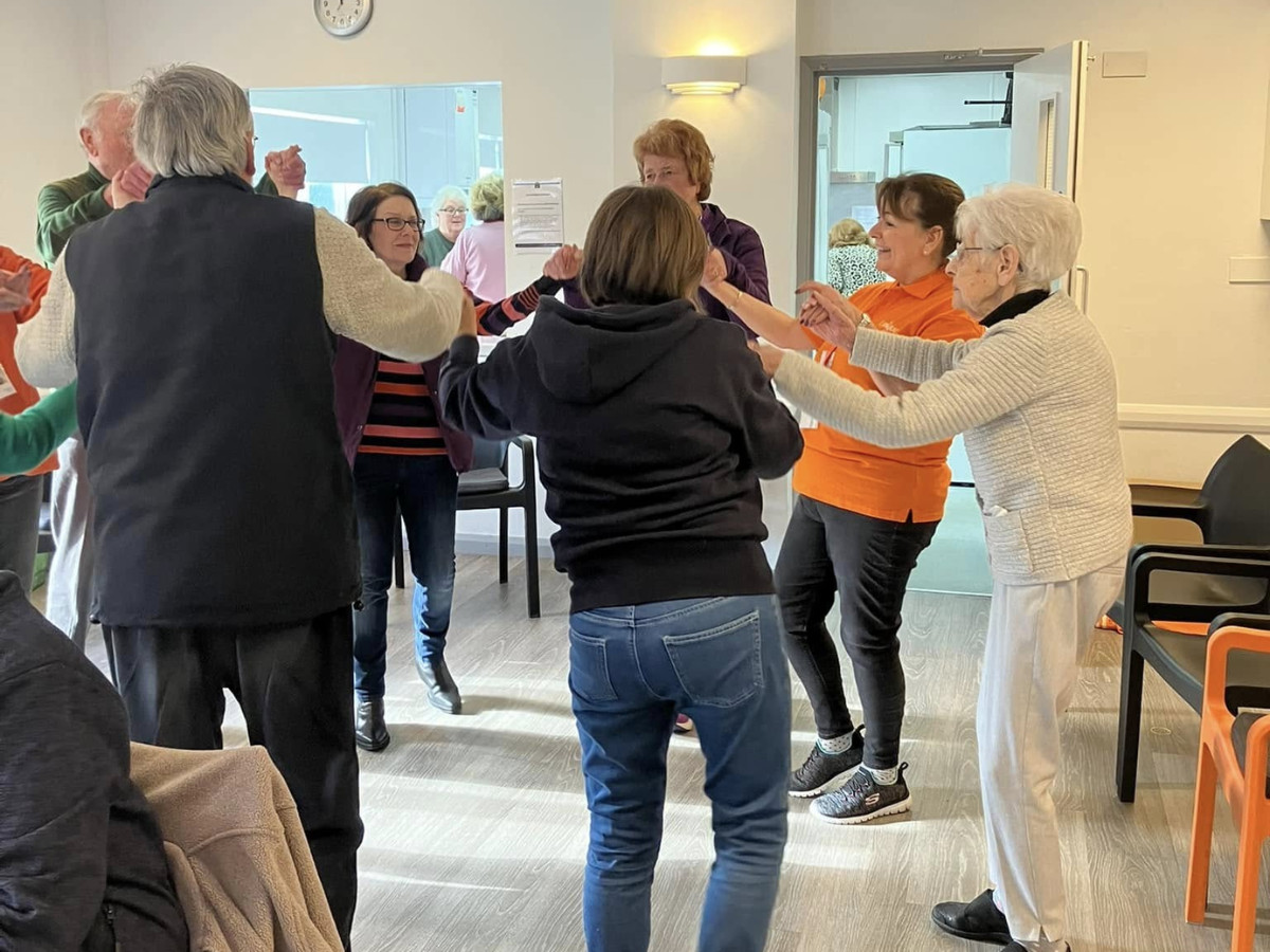 A group of people, mostly older adults, dancing in a circle at a memory café.