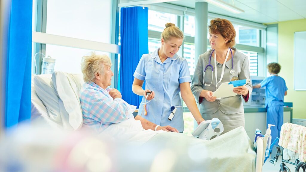 Older woman in hospital talking to a nurse and doctor during a ward round