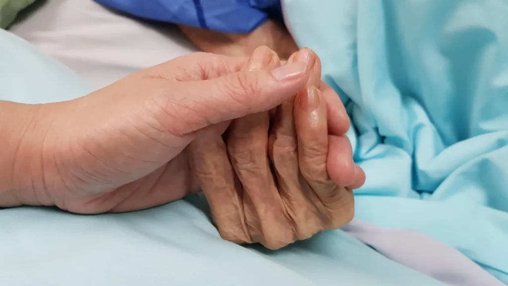 Two hands holding each other, on what looks like a hospital bed