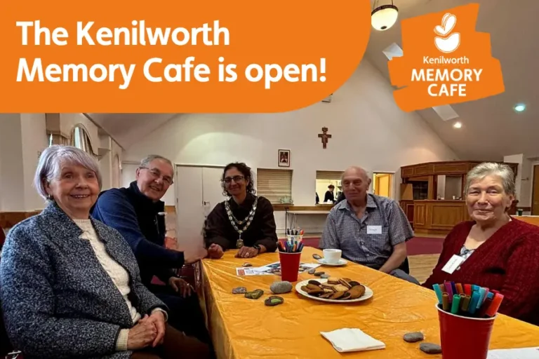 A group of attendees at the Kenilworth Memory Cafe opening, overlayed with the logo for the cafe and the text 'the Kenilworth Memory Cafe is Open'