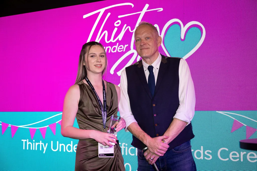 Kara Cae, registered manager at unique senior care being awarded the thirty under 30 award. she is stood next to a man on stage and the screen behind them says, 30 under 3thirty.