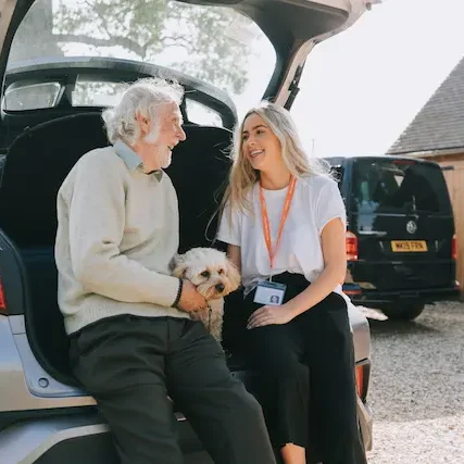 elderly man and carer sitting in the boot of car